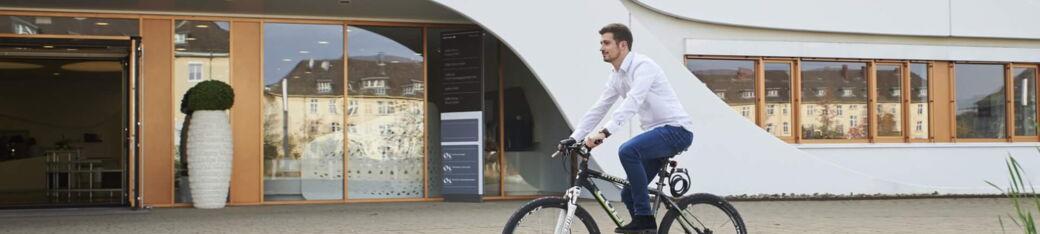 Mitarbeiter fährt Fahrrad vor dem Bürogebäude und nutzt Jobrad-Benefit