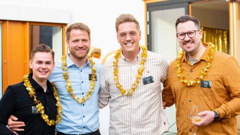 Lächelnde Kollegen mit goldfarbenen Hawaiiketten feiern gemeinsam bei einem Firmenevent