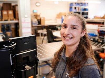 Lächelnde junge Technikerin in der Firmenwerkstatt in Arbeitskleidung