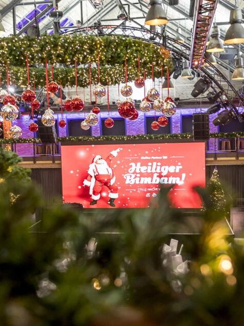 Festlich und weihnachtlich dekorierter Veranstaltungsraum und einem großen Bildschirm mit dem Schriftzug 'Heiliger Bimbam!' für die Firmenweihnachtsfeier von Kaffee Partner
