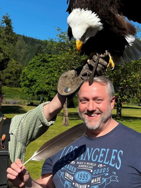 Sales Director mit einem Greifvogel auf dem Kopf, der von einem Falkner begleitet wird, bei einer einzigartigen Teamaktivität im Freien