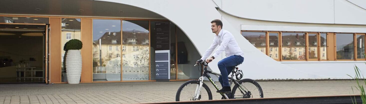 Mitarbeiter fährt Fahrrad vor dem Bürogebäude und nutzt Jobrad-Benefit
