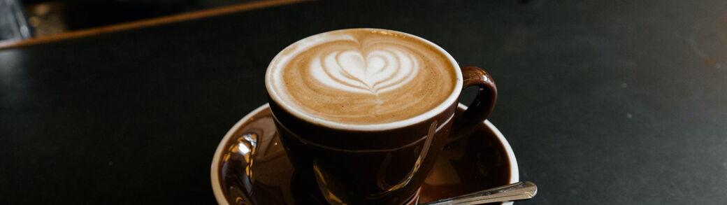 Eine Tasse Kaffee mit einem Herz Muster aus Milchschaum auf einem Tresen.