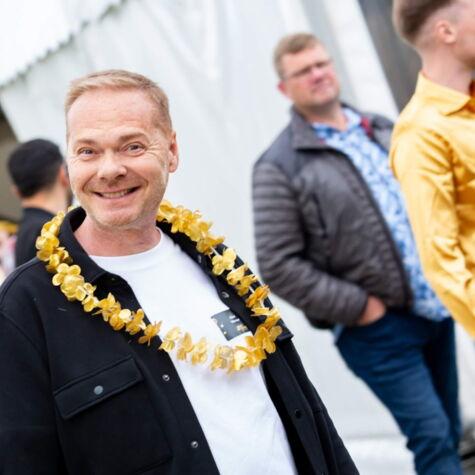 Lächelnder Kollege mit goldener Hawaiikette feiert auf einer Jubiläumsfeier des Unternehmens