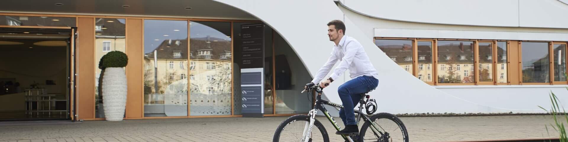 Mitarbeiter fährt Fahrrad vor dem Bürogebäude und nutzt Jobrad-Benefit